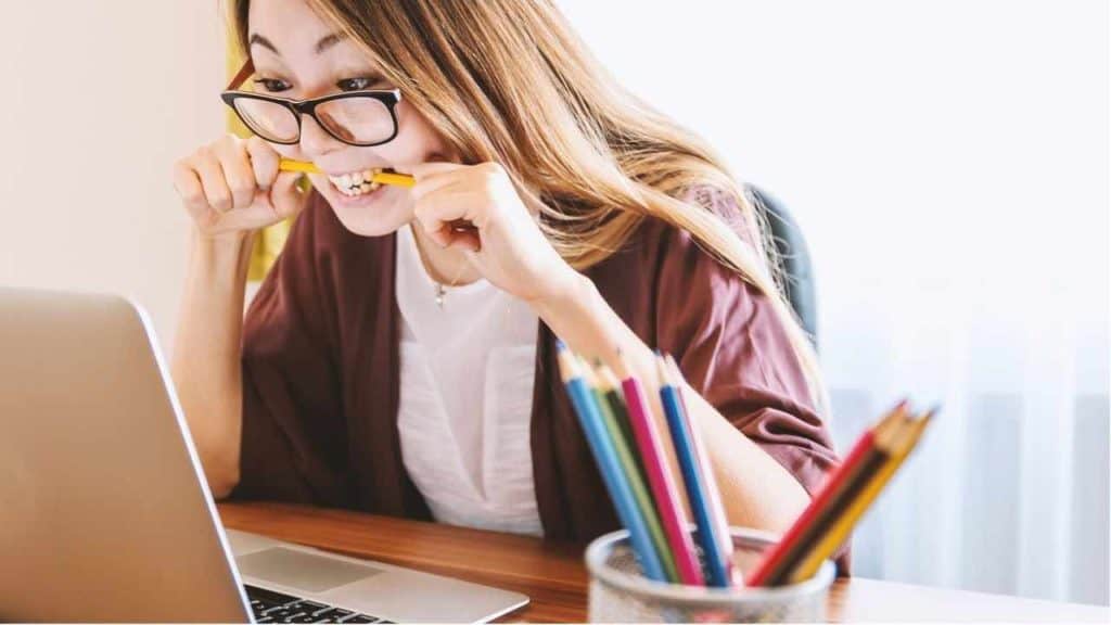 girl biting a pen in front of her laptop